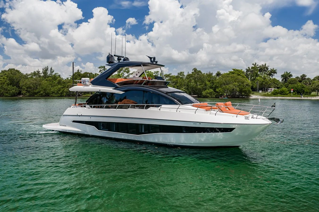 A sleek and modern yacht cruises gracefully on calm, emerald waters under a bright, partly cloudy sky. aboard ELENA Yacht for Sale