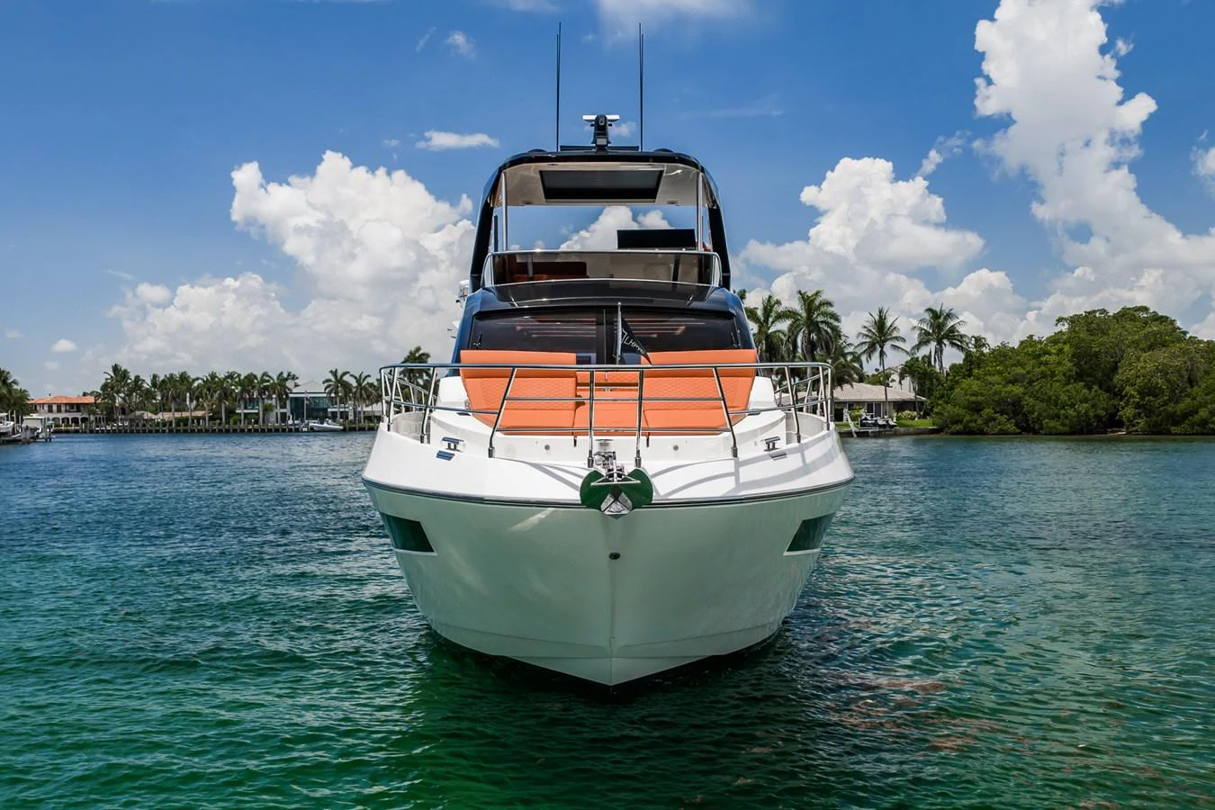 A sleek yacht is anchored in calm waters, showcasing its modern design against a backdrop of lush greenery and a clear blue sky. aboard ELENA Yacht for Sale