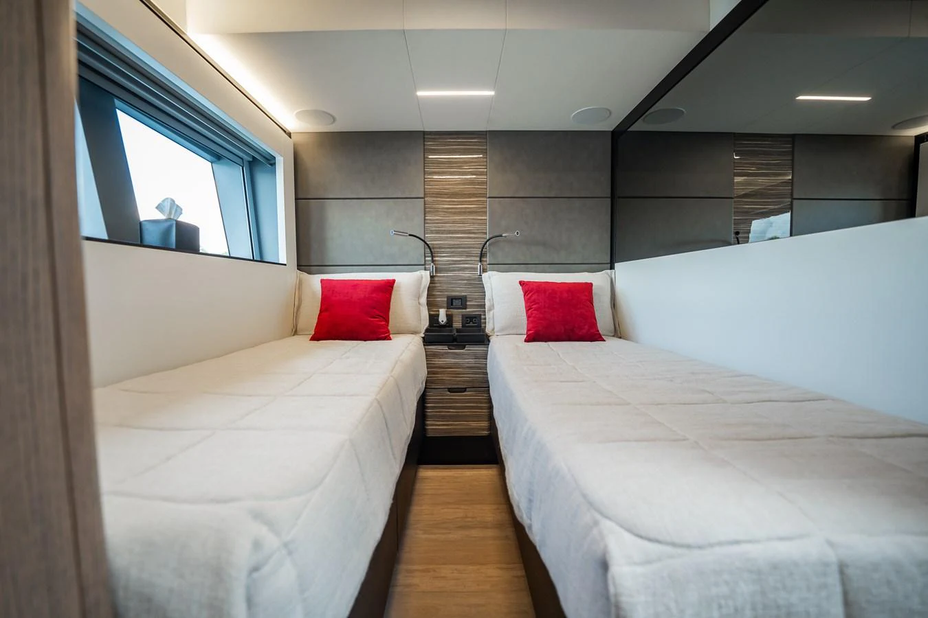 The twin stateroom features two comfortable single beds with plush bedding and vibrant red accent pillows. aboard ELENA Yacht for Sale