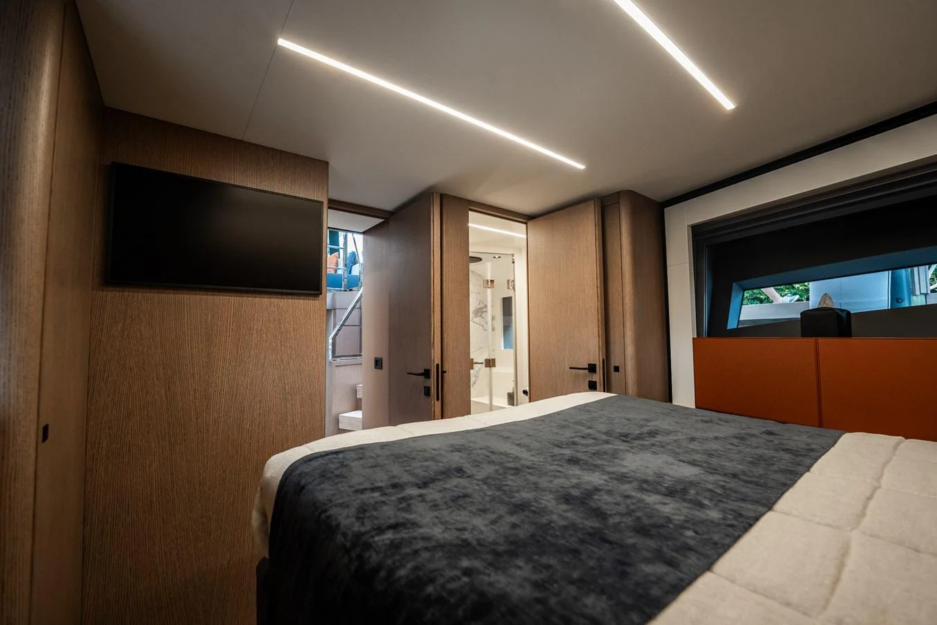 A modern stateroom featuring a comfortable bed, sleek wood paneling, and a flat-screen TV. aboard ELENA Yacht for Sale