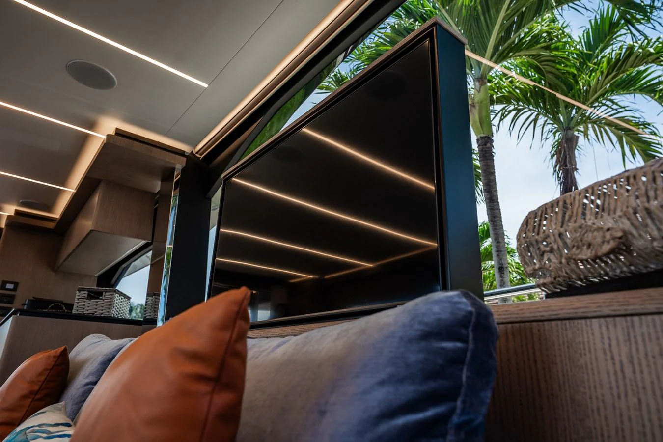 A luxurious interior space featuring a large television and plush seating with a view of palm trees outside. aboard ELENA Yacht for Sale