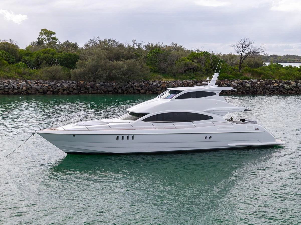 A sleek white yacht glides gracefully on calm waters with a lush green shoreline in the background. aboard WARREN 87 Yacht for Sale