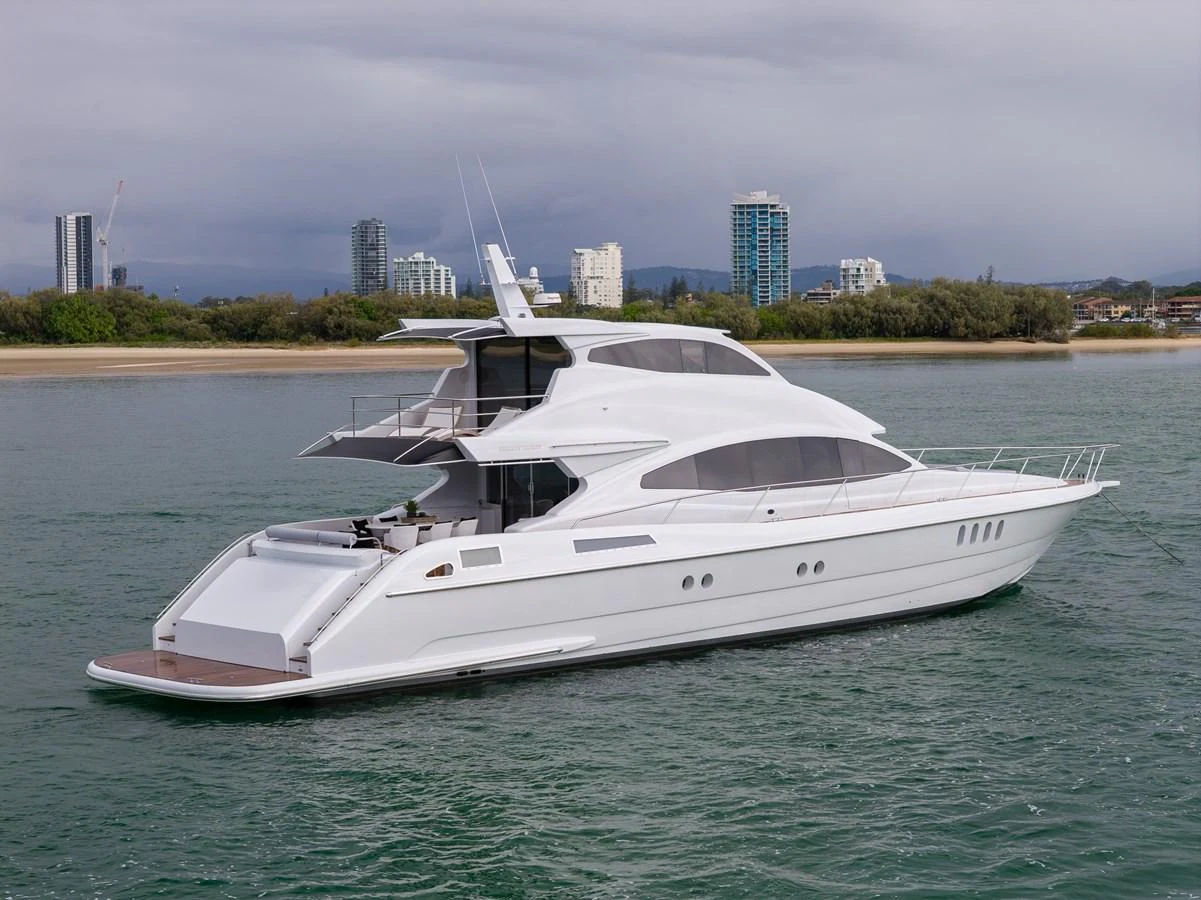 A sleek, modern yacht cruising near the shoreline with a cityscape in the background. aboard WARREN 87 Yacht for Sale