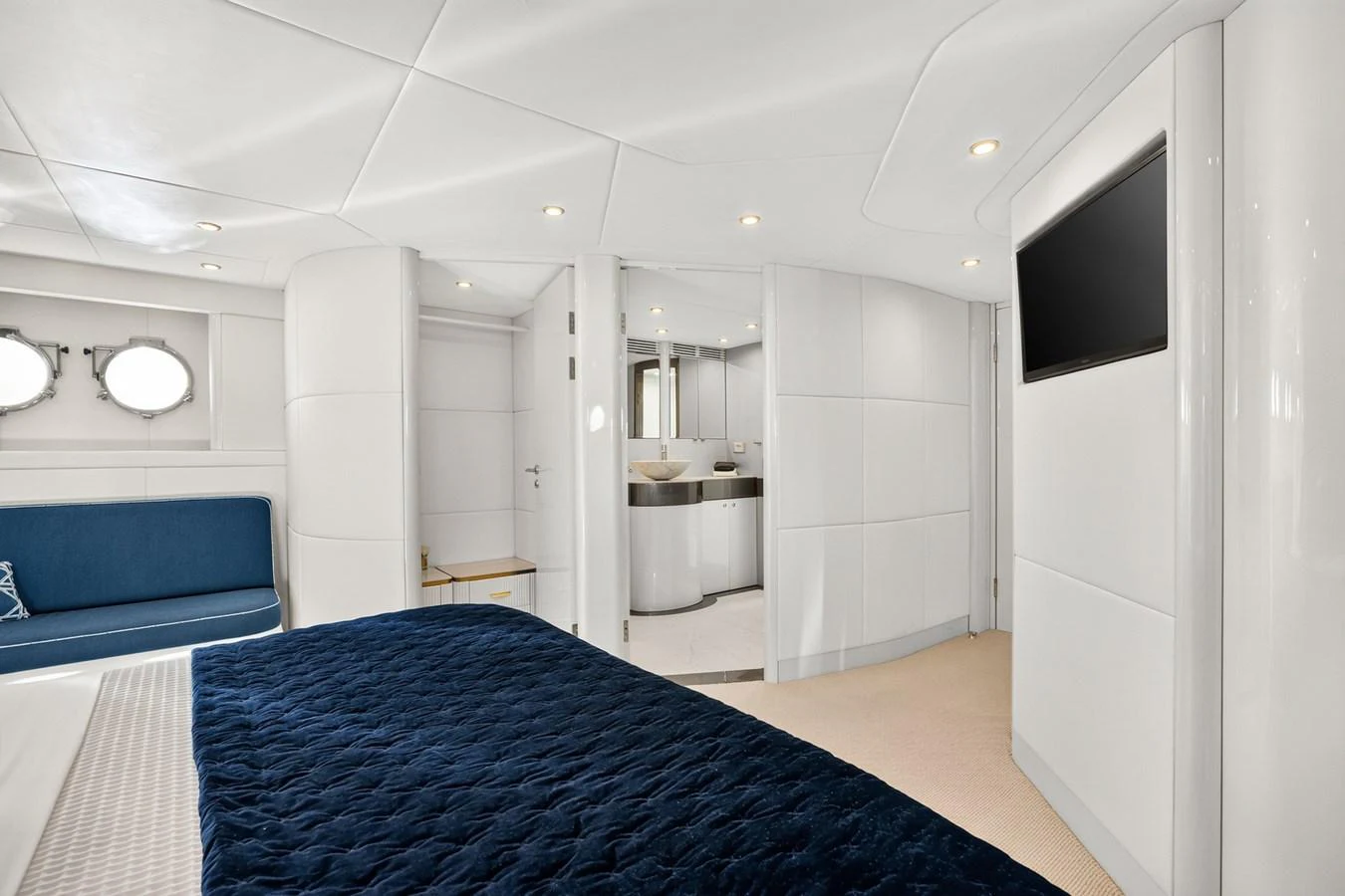 The stateroom features a luxurious bed with a navy blue quilt, a seating area, and an ensuite bathroom. aboard WARREN 87 Yacht for Sale