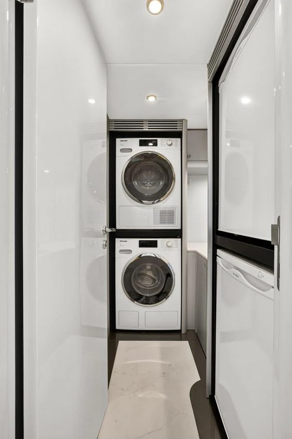 The yacht features a modern and efficient laundry room with stacked washer and dryer units. aboard WARREN 87 Yacht for Sale