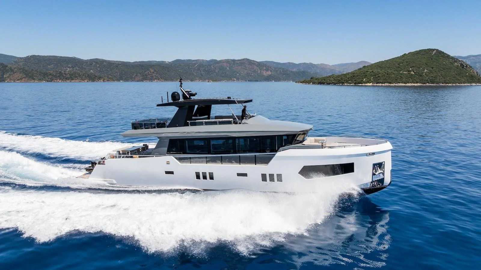 A sleek and modern yacht cruises through clear blue waters against a scenic backdrop. aboard FERRO 77 Yacht for Sale