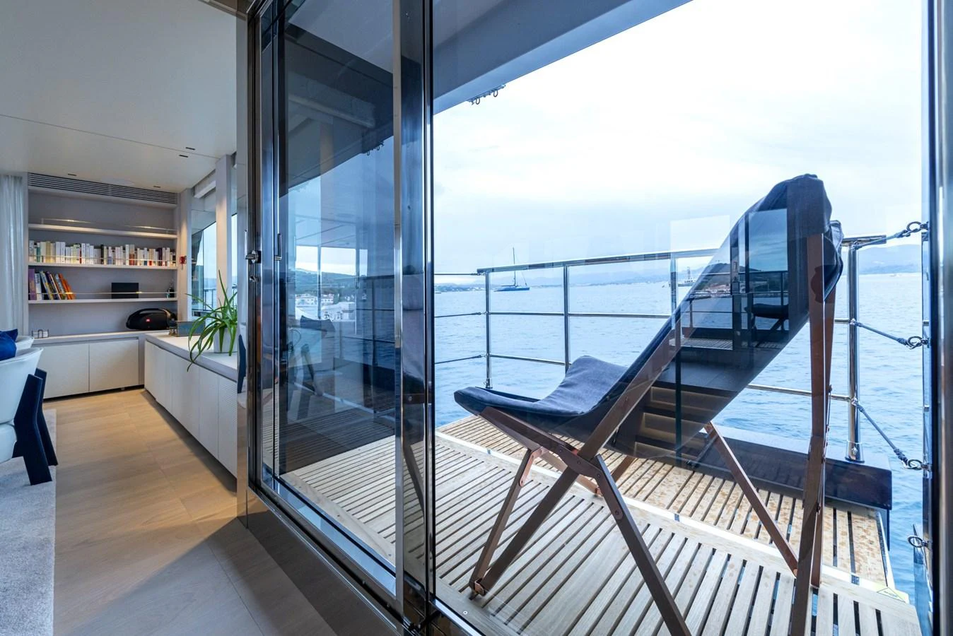 The salon opens up to a serene view of the water, featuring a comfortable lounge chair on the deck. aboard AMER 120/11 Yacht for Sale