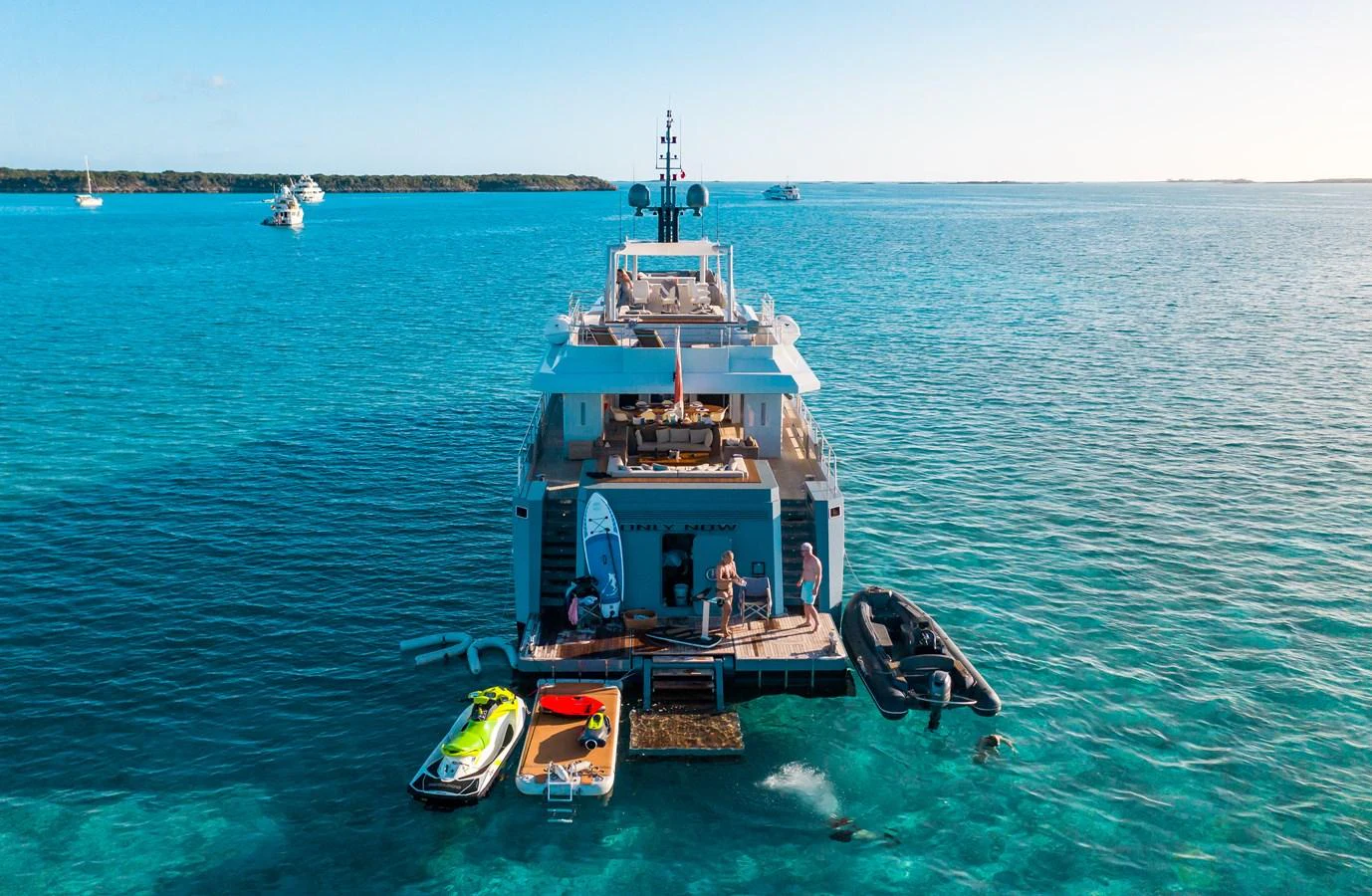 The yacht's aft deck is bustling with activity, featuring water toys and a tender in a serene blue sea setting. aboard ONLY NOW Yacht for Sale