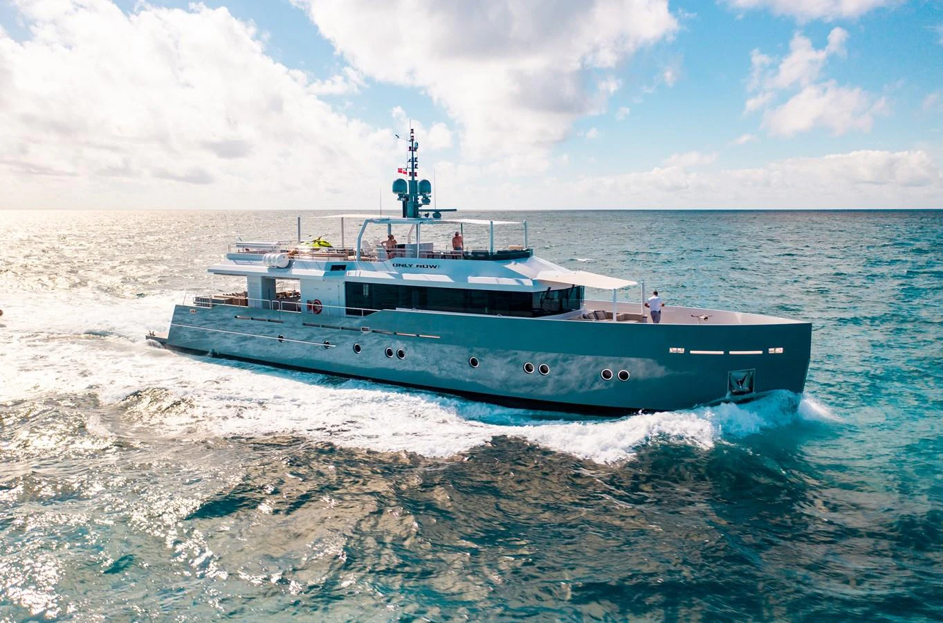 A sleek and modern yacht cruises through the open sea under a bright sky. aboard ONLY NOW Yacht for Sale