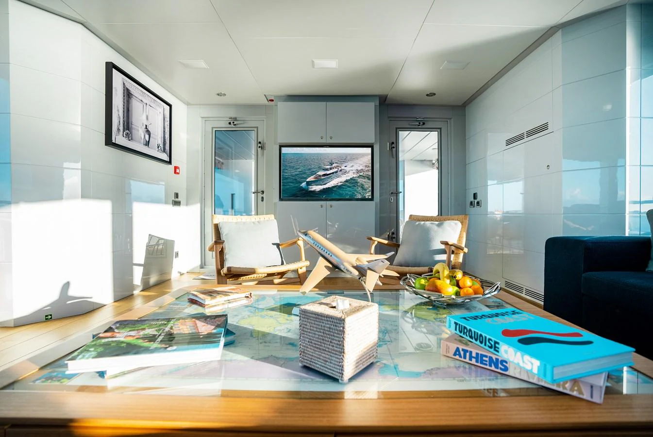 A bright and modern yacht interior with comfortable seating and a large table adorned with books and fruit. aboard ONLY NOW Yacht for Sale