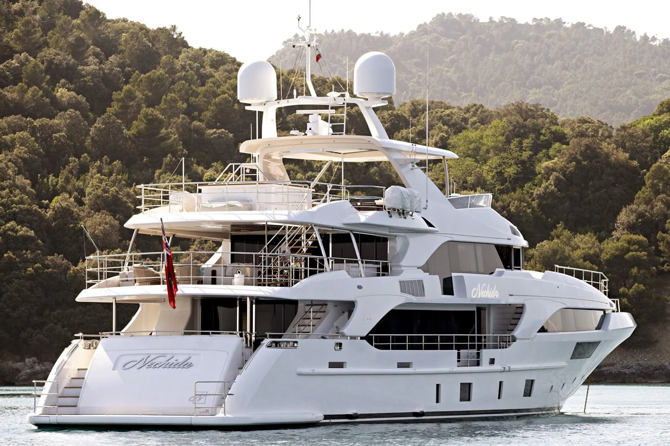 A luxurious yacht anchored in a serene bay with lush green hills in the background. aboard NECHIDA Yacht for Sale