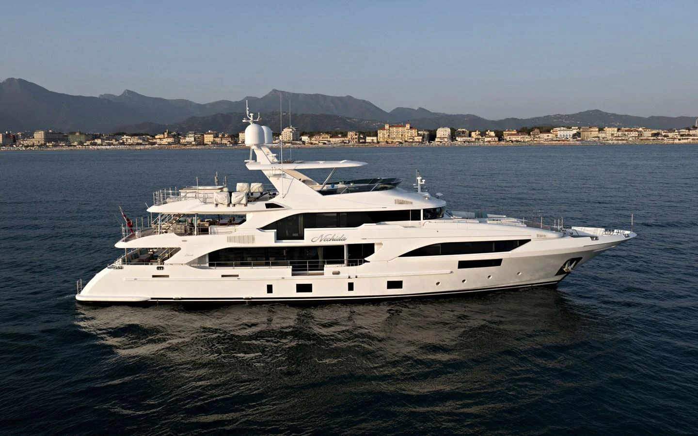 A sleek and modern yacht cruising on calm waters with a scenic coastal backdrop. aboard NECHIDA Yacht for Sale