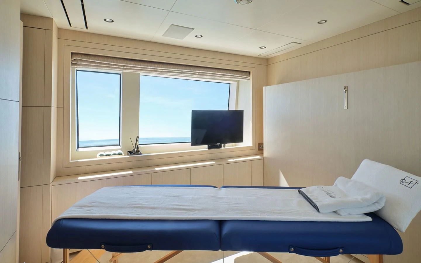 The yacht features a serene spa room with a massage table and a large window offering a view of the sea. aboard NECHIDA Yacht for Sale