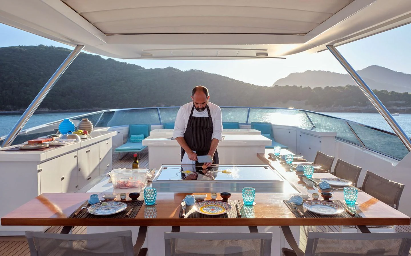 An inviting alfresco dining area with a chef preparing a meal, set against a scenic backdrop. aboard NECHIDA Yacht for Sale