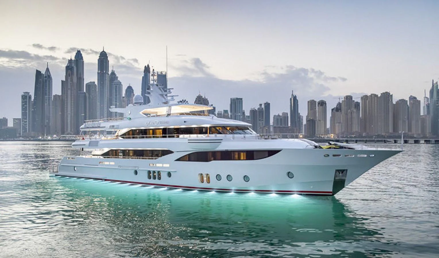 A luxurious yacht is anchored in a serene harbor with a stunning city skyline in the background. aboard ATLANTIS Yacht for Sale