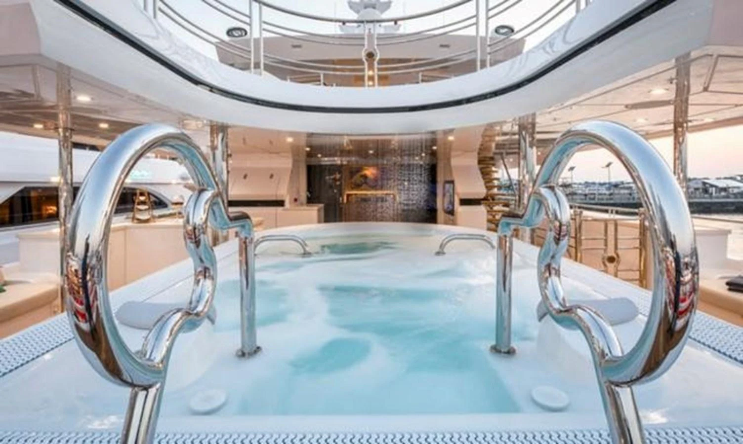 The yacht features a luxurious jacuzzi area with sleek chrome handrails and ample seating. aboard ATLANTIS Yacht for Sale