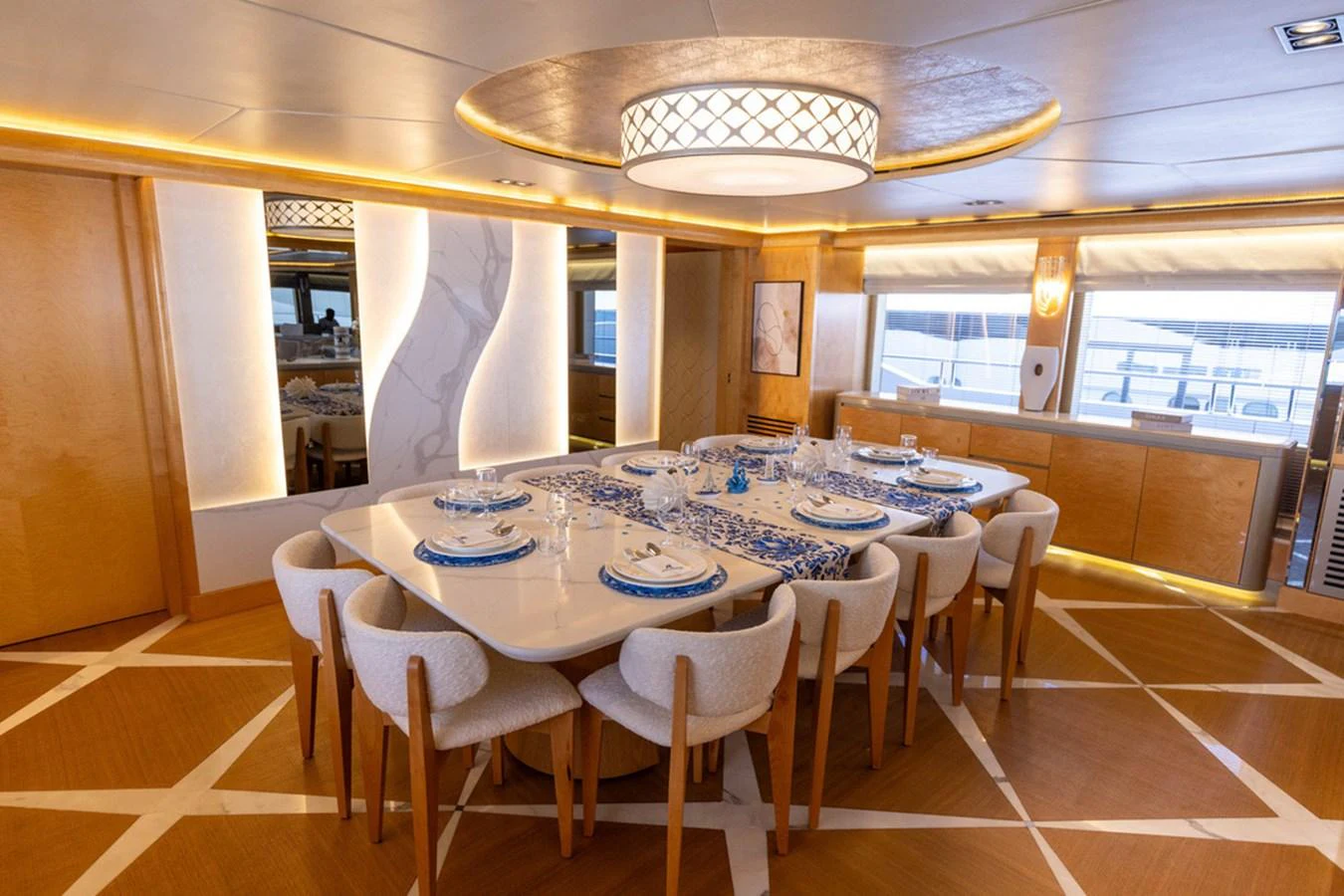 The yacht's dining area features a large, elegant table set for a meal, surrounded by comfortable chairs and illuminated by a stylish overhead light fixture. aboard ATLANTIS Yacht for Sale