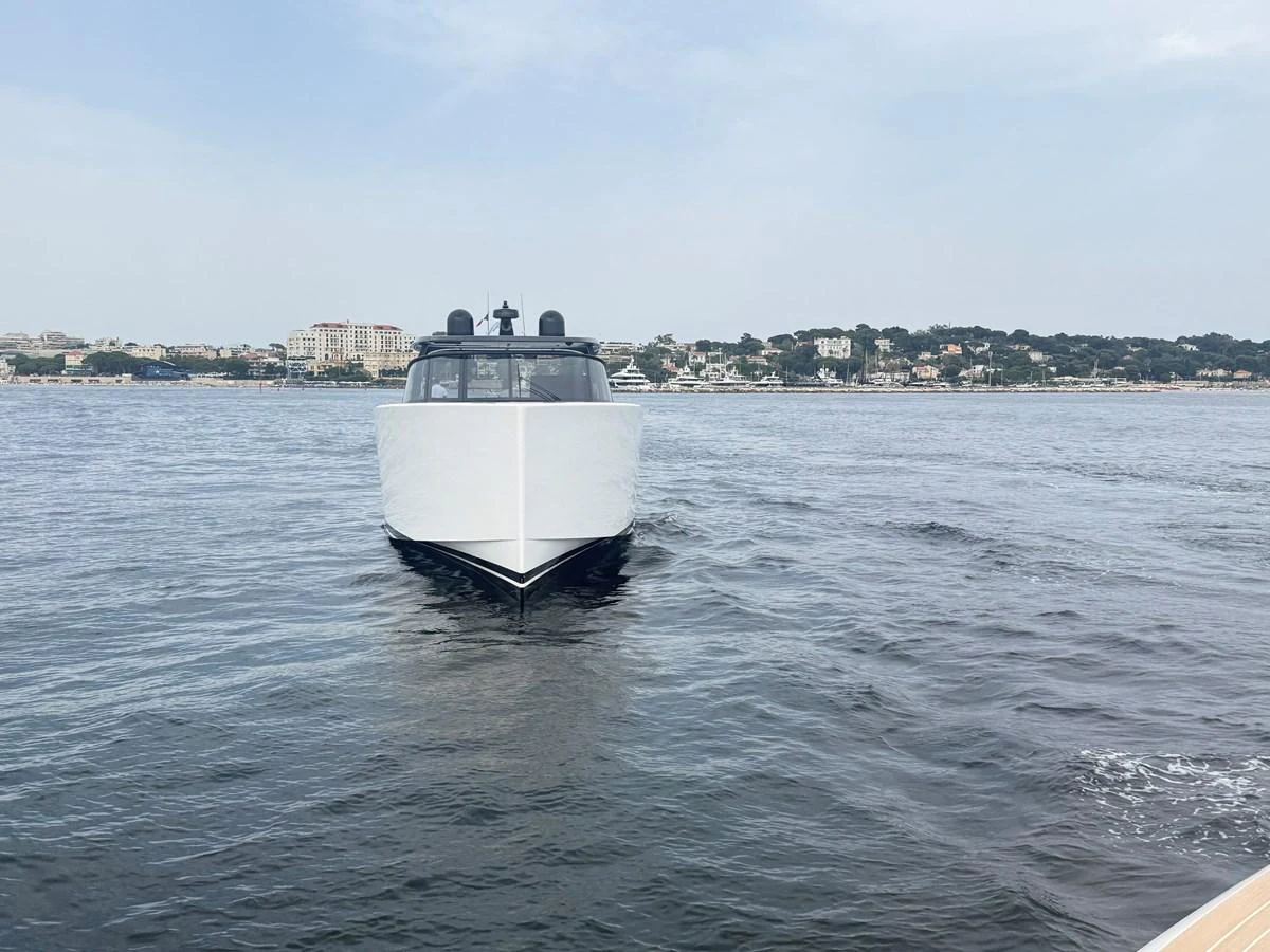 A sleek yacht is seen head-on, cruising on calm waters with a coastal town in the background. aboard DUTCH PEARL Yacht for Sale