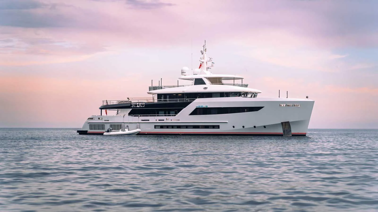 A sleek and modern yacht is anchored on calm waters under a pastel sky. aboard HEEUS Yacht for Sale