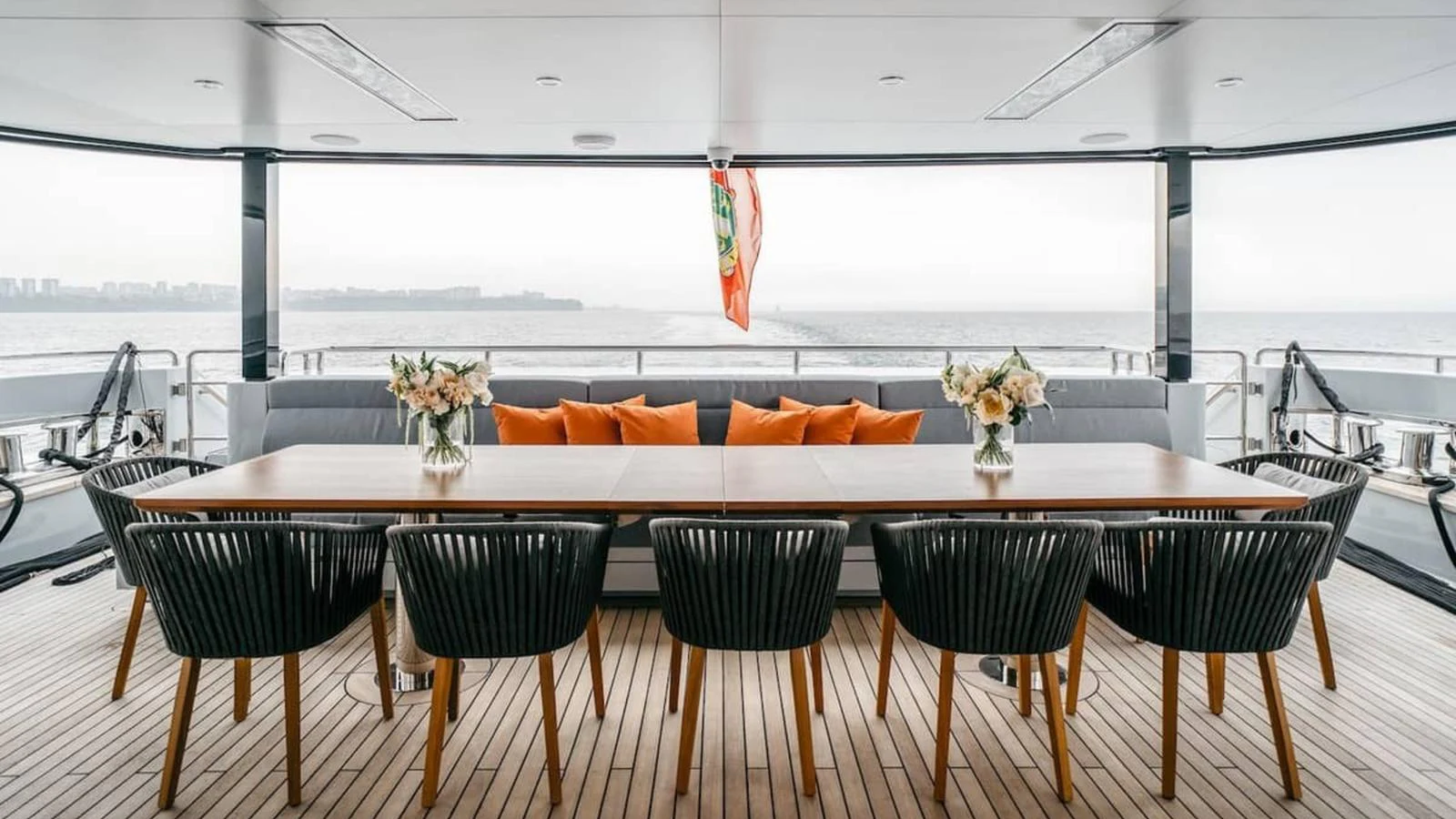 The aft deck features an elegant dining area with a long table and stylish chairs, perfect for alfresco dining with a view. aboard HEEUS Yacht for Sale