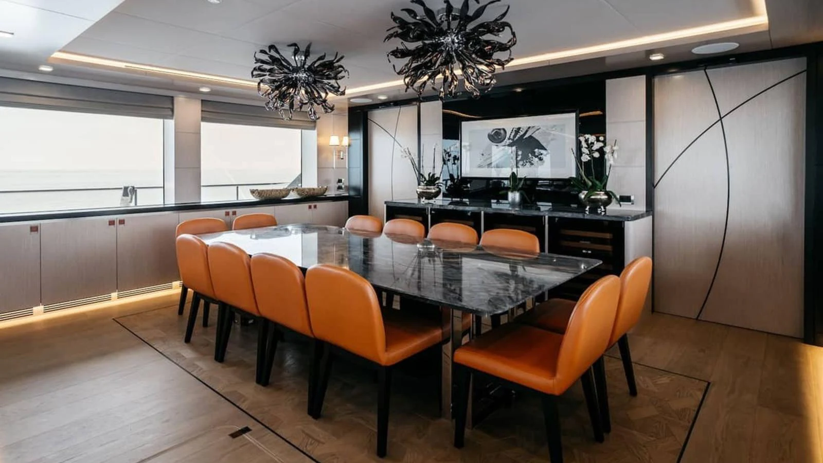 The yacht's dining area features a sleek table with vibrant orange chairs and modern lighting fixtures. aboard HEEUS Yacht for Sale