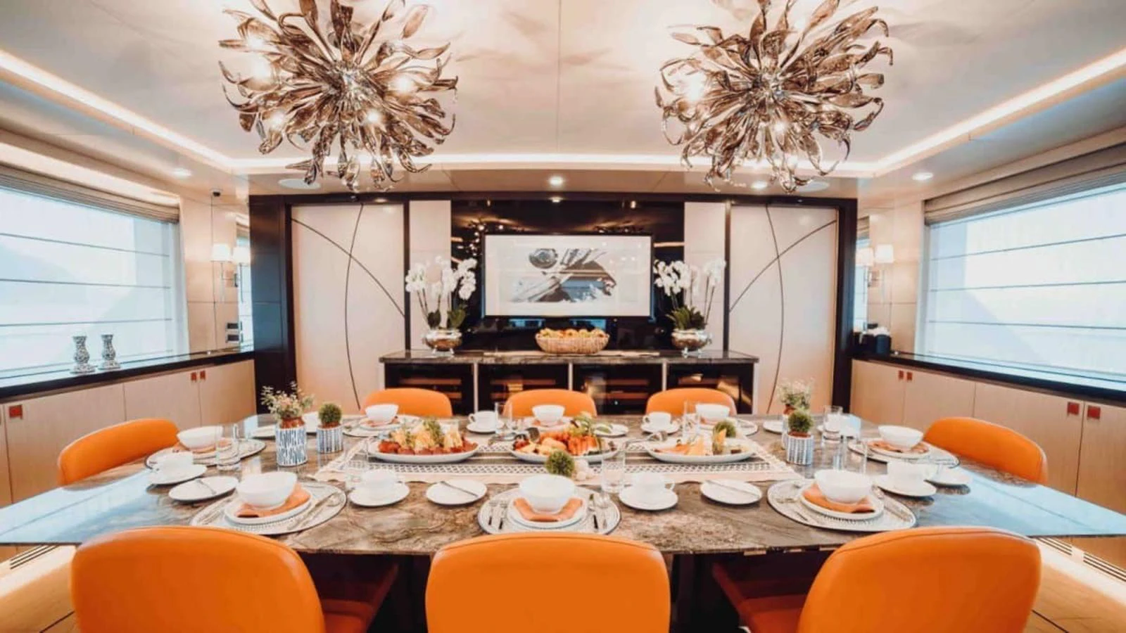 The yacht's dining area features a lavishly set table with vibrant orange chairs and elegant lighting fixtures. aboard HEEUS Yacht for Sale
