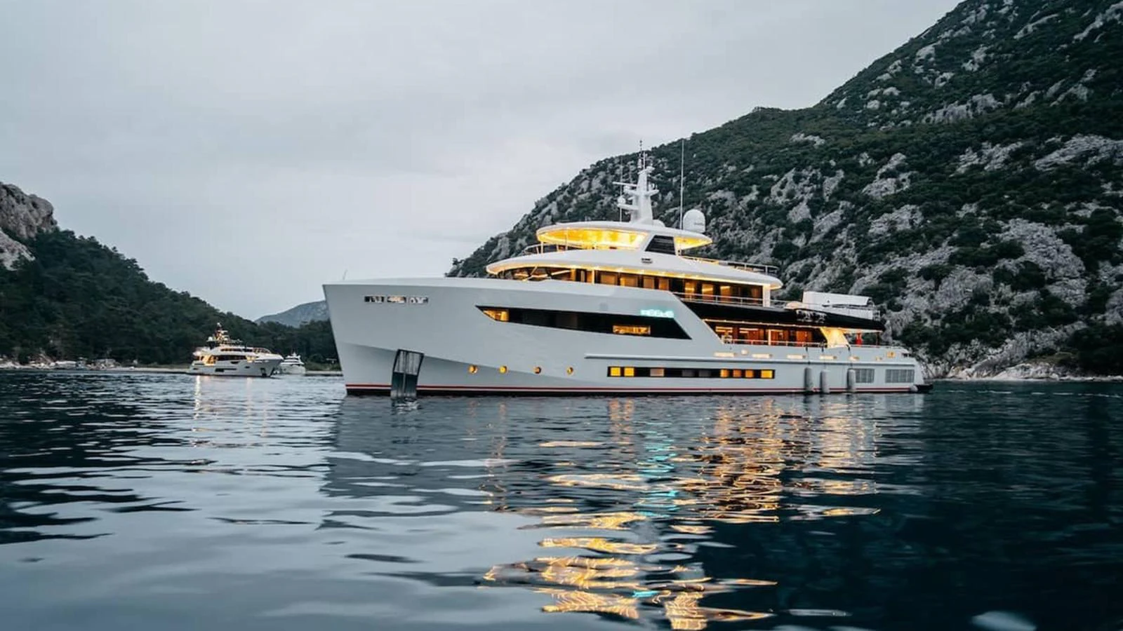 A luxurious yacht is anchored in a serene bay surrounded by lush hills. aboard HEEUS Yacht for Sale