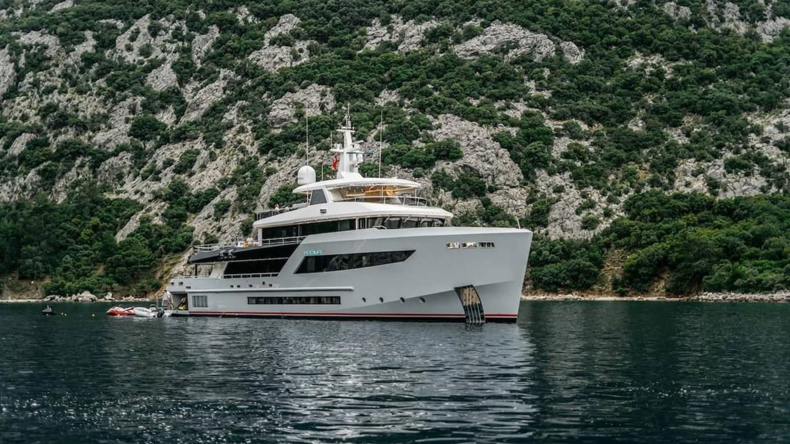 A luxurious yacht is anchored in a serene bay surrounded by lush green hills. aboard HEEUS Yacht for Sale