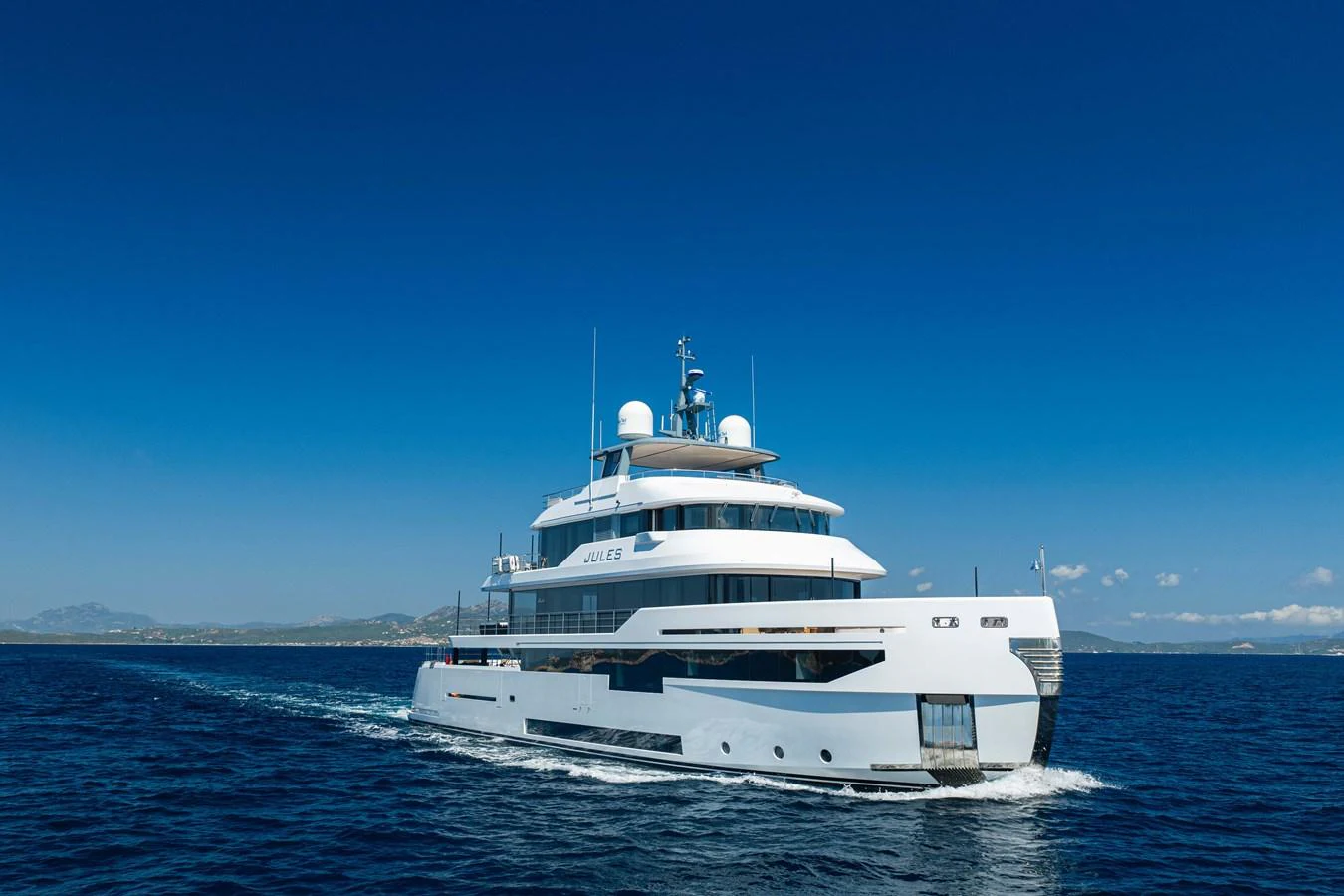 A sleek, modern yacht cruising on open waters under a clear blue sky. aboard JULES Yacht for Sale