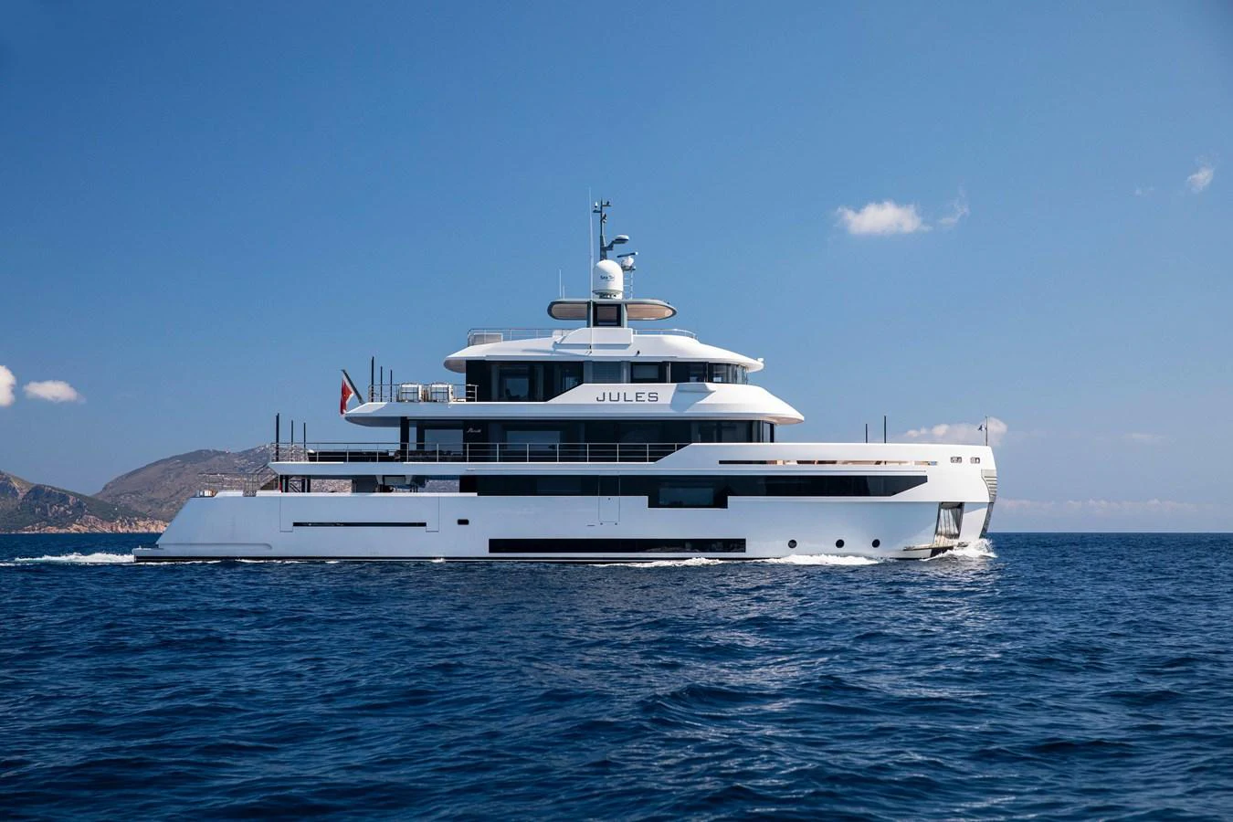 A sleek, modern yacht cruises through calm blue waters under a clear sky. aboard JULES Yacht for Sale
