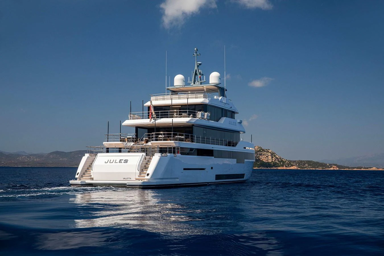 A luxurious yacht cruising on calm waters under a clear blue sky. aboard JULES Yacht for Sale