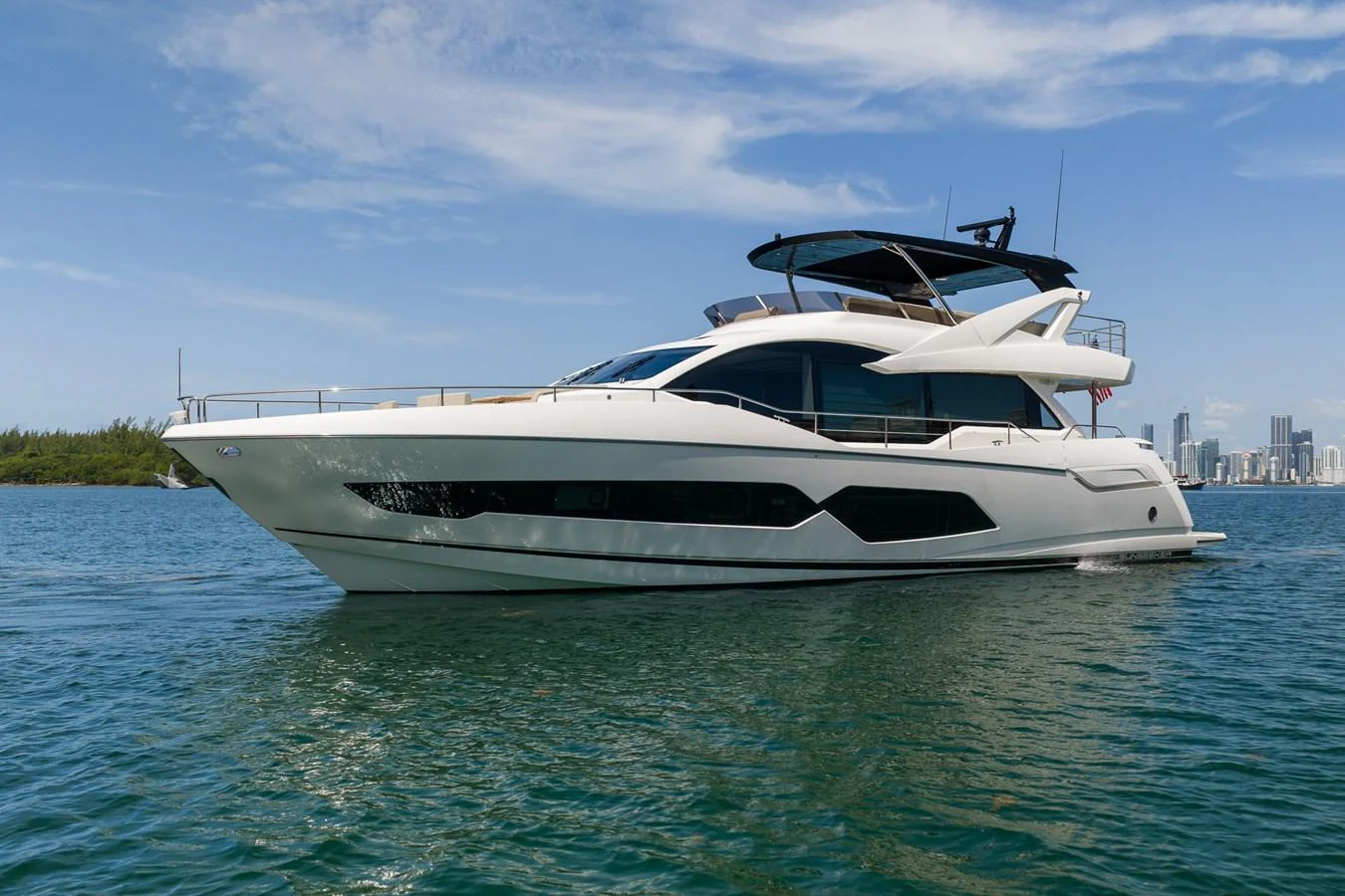 A sleek and modern yacht cruising on calm waters with a city skyline in the background. aboard BAZINGA Yacht for Sale