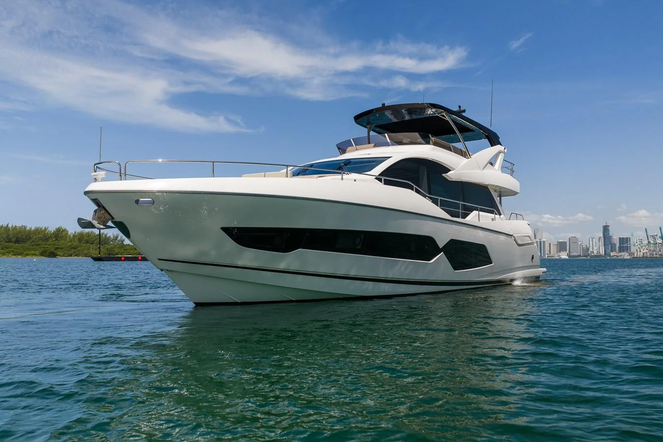 A sleek and modern yacht cruises gracefully on calm waters with a cityscape in the background. aboard BAZINGA Yacht for Sale