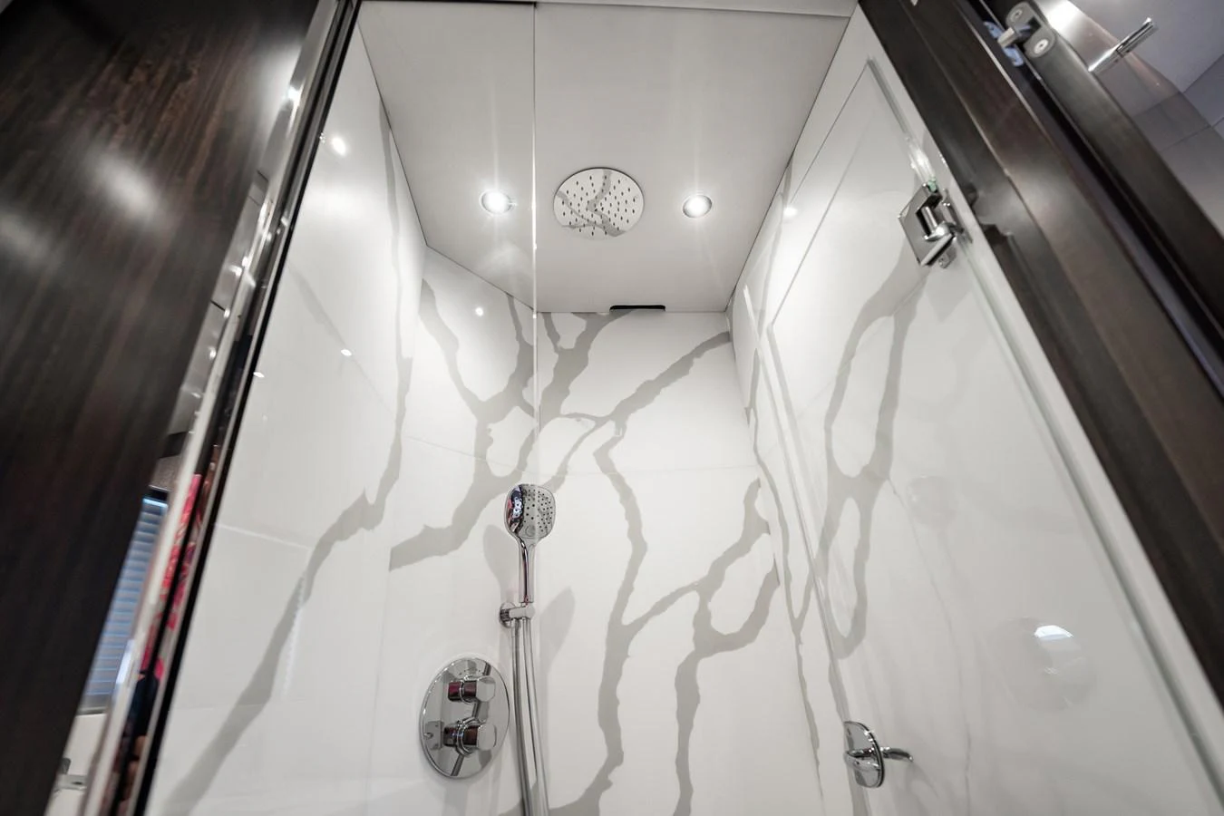 A modern and luxurious shower with sleek fixtures and elegant marble-patterned walls. aboard BAZINGA Yacht for Sale