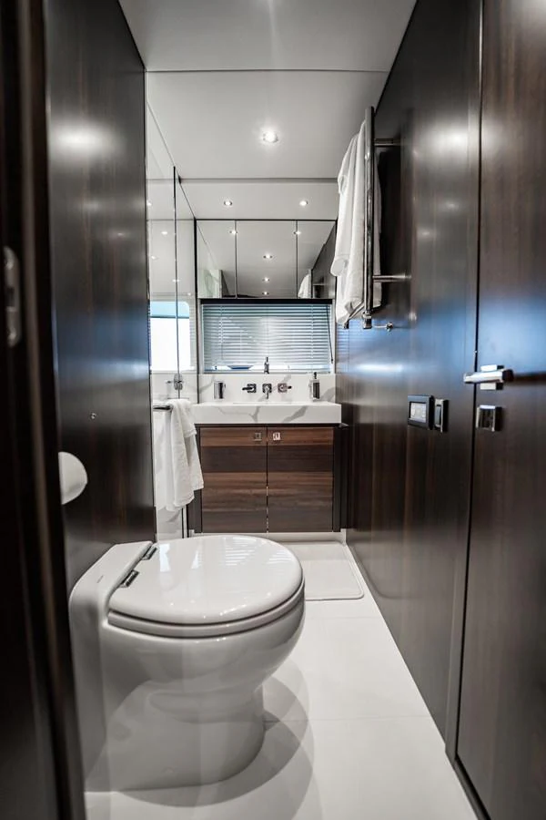 A sleek and modern yacht bathroom with dark wood paneling and a pristine white toilet and sink. aboard BAZINGA Yacht for Sale