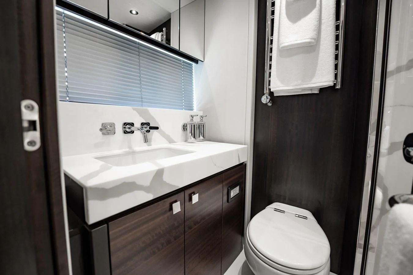 A sleek and modern yacht bathroom with dark wood accents and a pristine white countertop. aboard BAZINGA Yacht for Sale