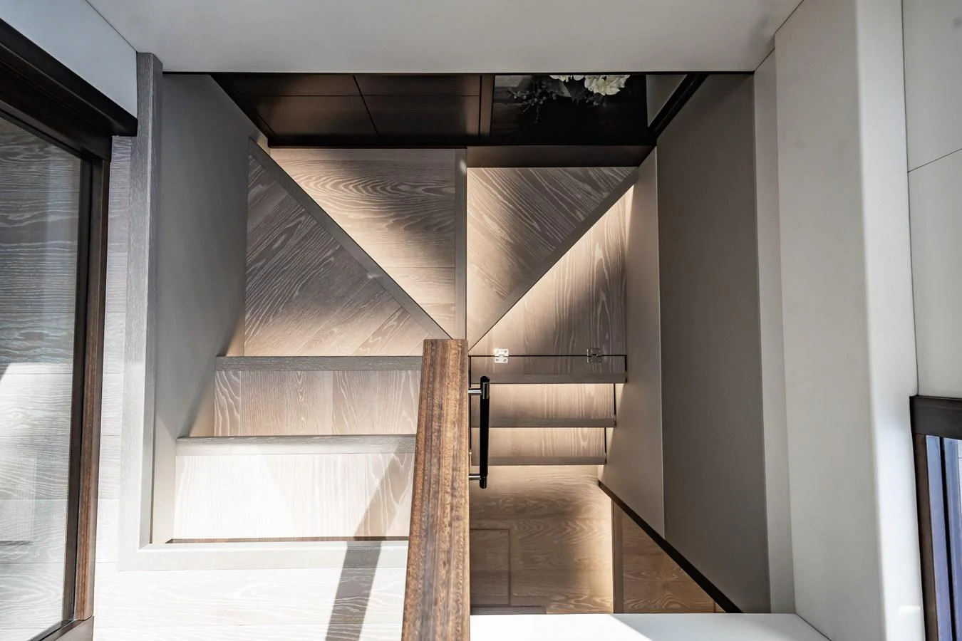 A modern staircase with sleek wooden finishes and ambient lighting. aboard BAZINGA Yacht for Sale