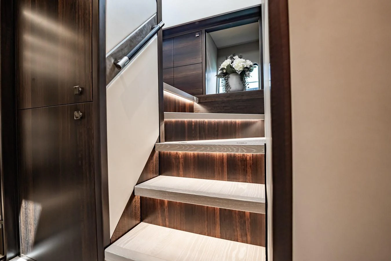 A stylish staircase with wooden steps and subtle lighting leads to the upper deck. aboard BAZINGA Yacht for Sale