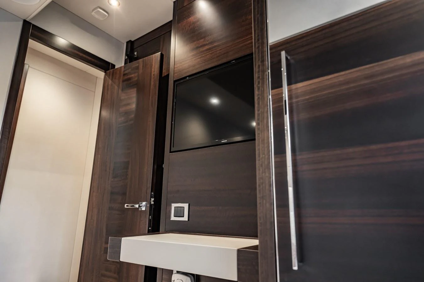 The image showcases a sleek and modern interior space with dark wood paneling and a built-in television. aboard BAZINGA Yacht for Sale