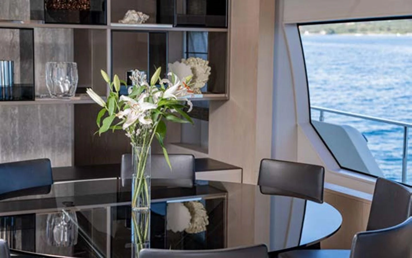 The yacht's dining area features a sleek black table with a beautiful floral arrangement, set against a backdrop of open shelving and a large window with a sea view. aboard E3 Yacht for Sale