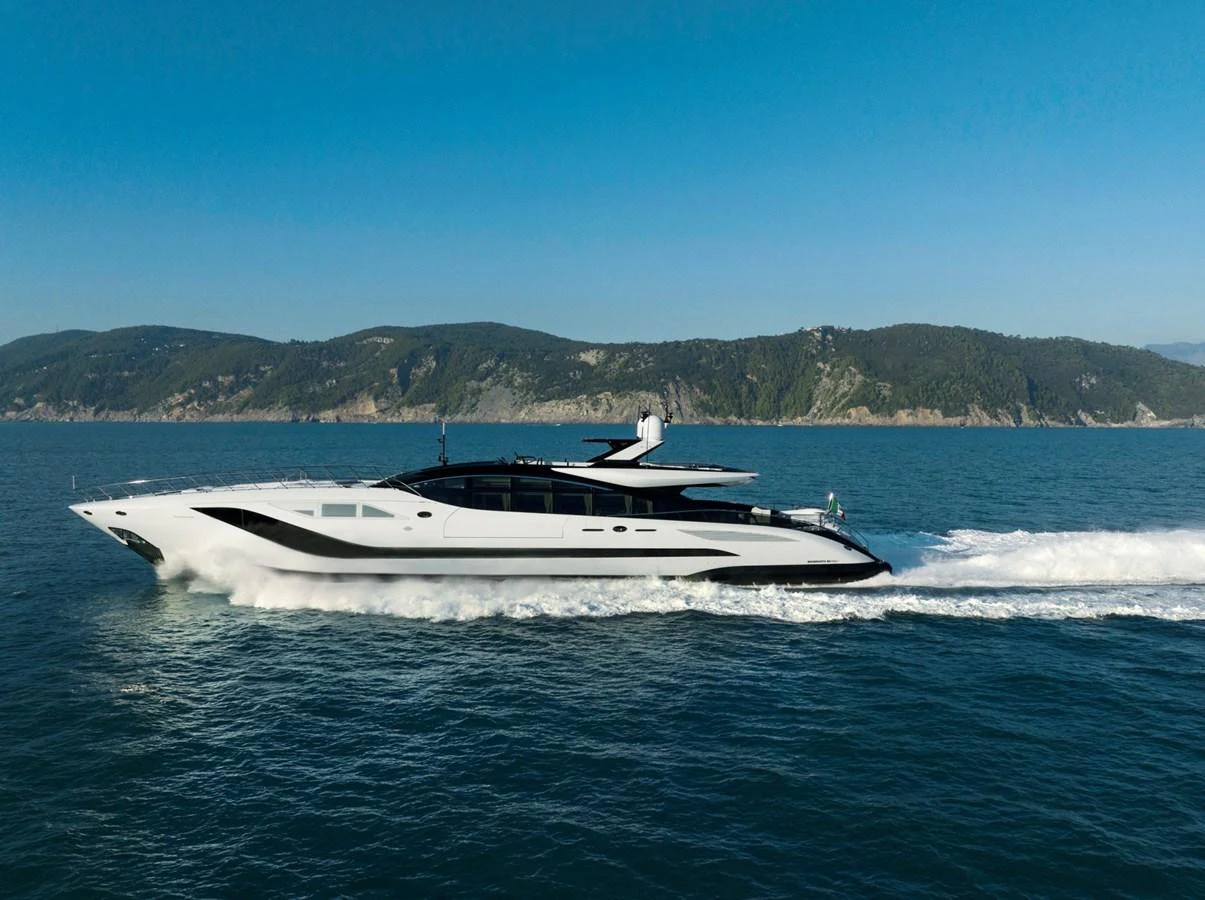 A sleek and modern yacht glides swiftly across the water with a scenic coastline in the background. aboard REBELLIOUS Yacht for Sale
