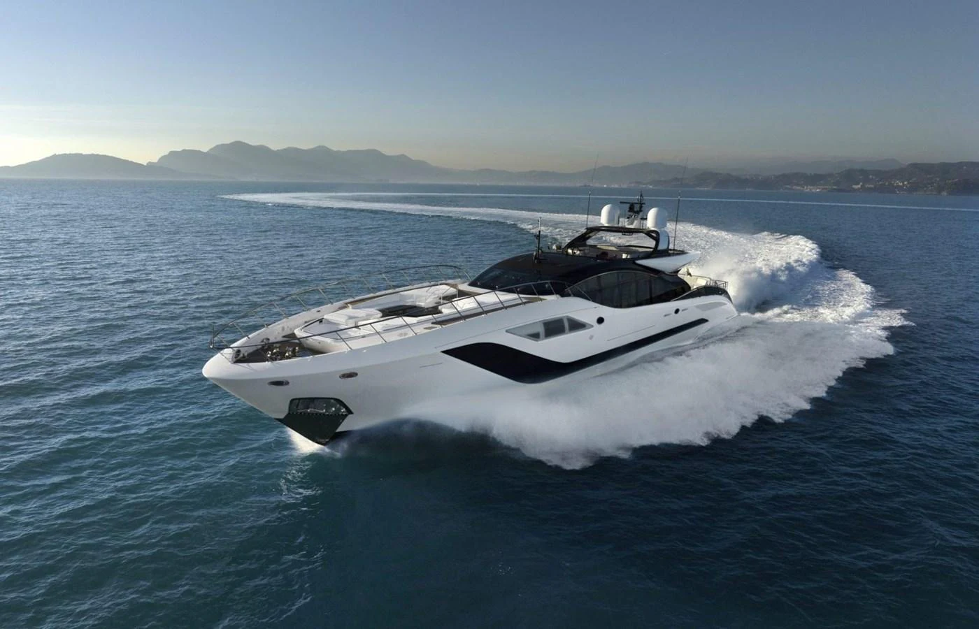 A sleek and modern yacht cruises swiftly across calm waters with a stunning backdrop of distant mountains. aboard REBELLIOUS Yacht for Sale