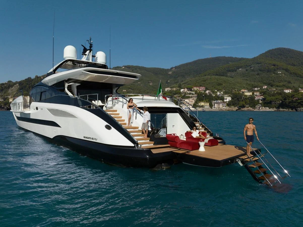 A luxurious yacht with a spacious aft deck featuring sun loungers and a swim platform, cruising in clear blue waters. aboard REBELLIOUS Yacht for Sale