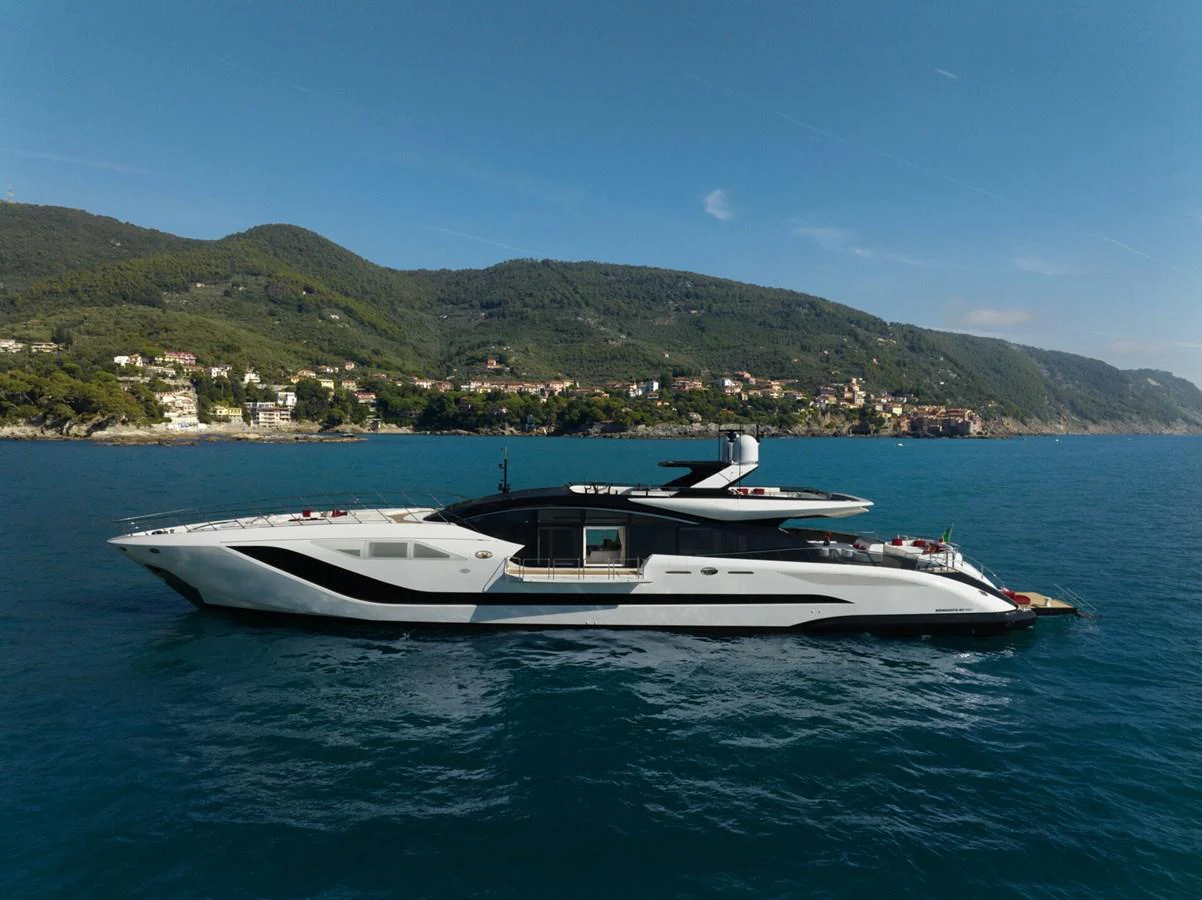 A sleek and modern yacht glides gracefully on calm blue waters with a scenic coastal backdrop. aboard REBELLIOUS Yacht for Sale