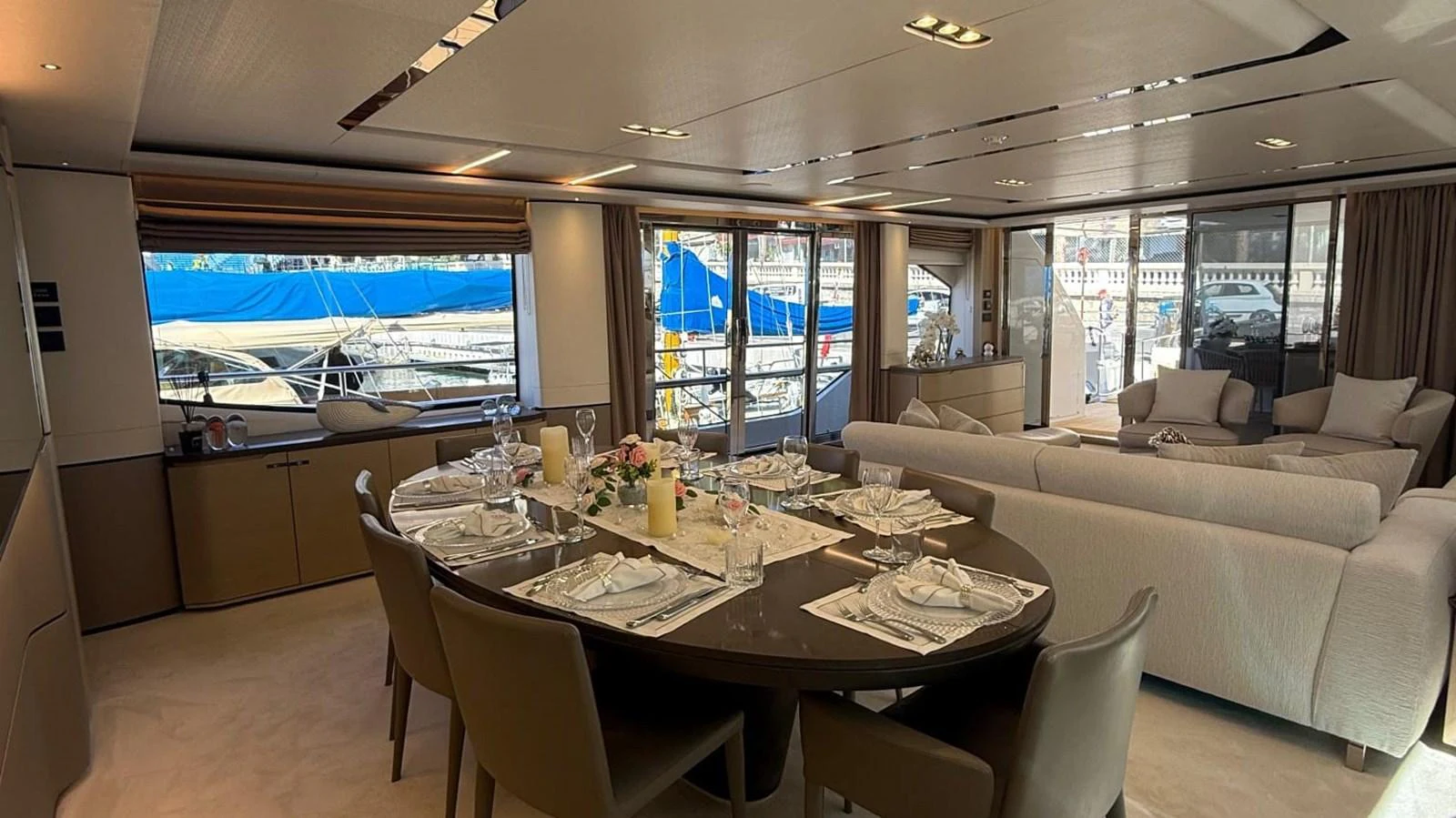 The yacht's dining area features a sophisticated table setting with a view of the marina through large windows. aboard ADROMELIA Yacht for Sale