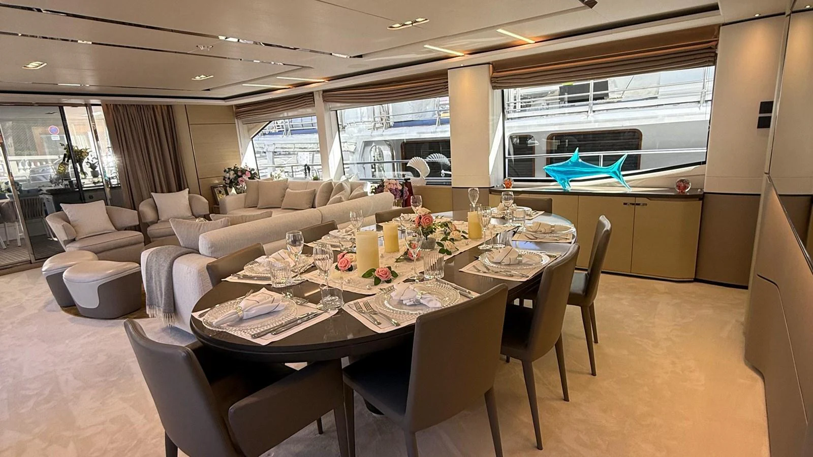 The yacht's dining area features an elegant table set for a meal, surrounded by comfortable seating and large windows offering a view of the marina. aboard ADROMELIA Yacht for Sale