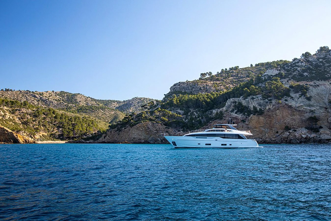 A sleek yacht cruises along a picturesque coastline with clear blue waters and rugged cliffs. aboard SEVEN Yacht for Sale