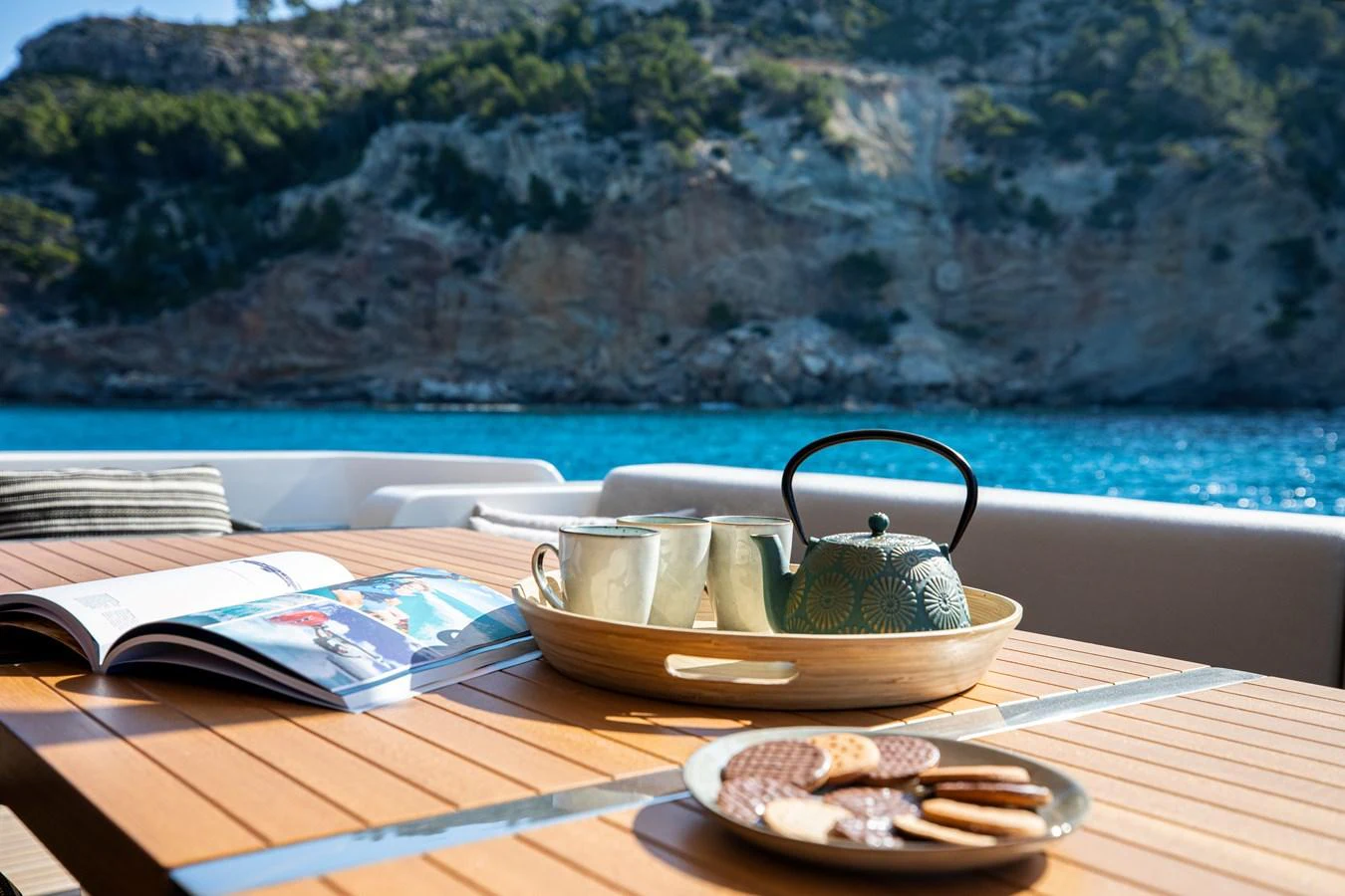 A serene aft deck setup with a tea set and snacks, overlooking a picturesque coastal landscape. aboard SEVEN Yacht for Sale