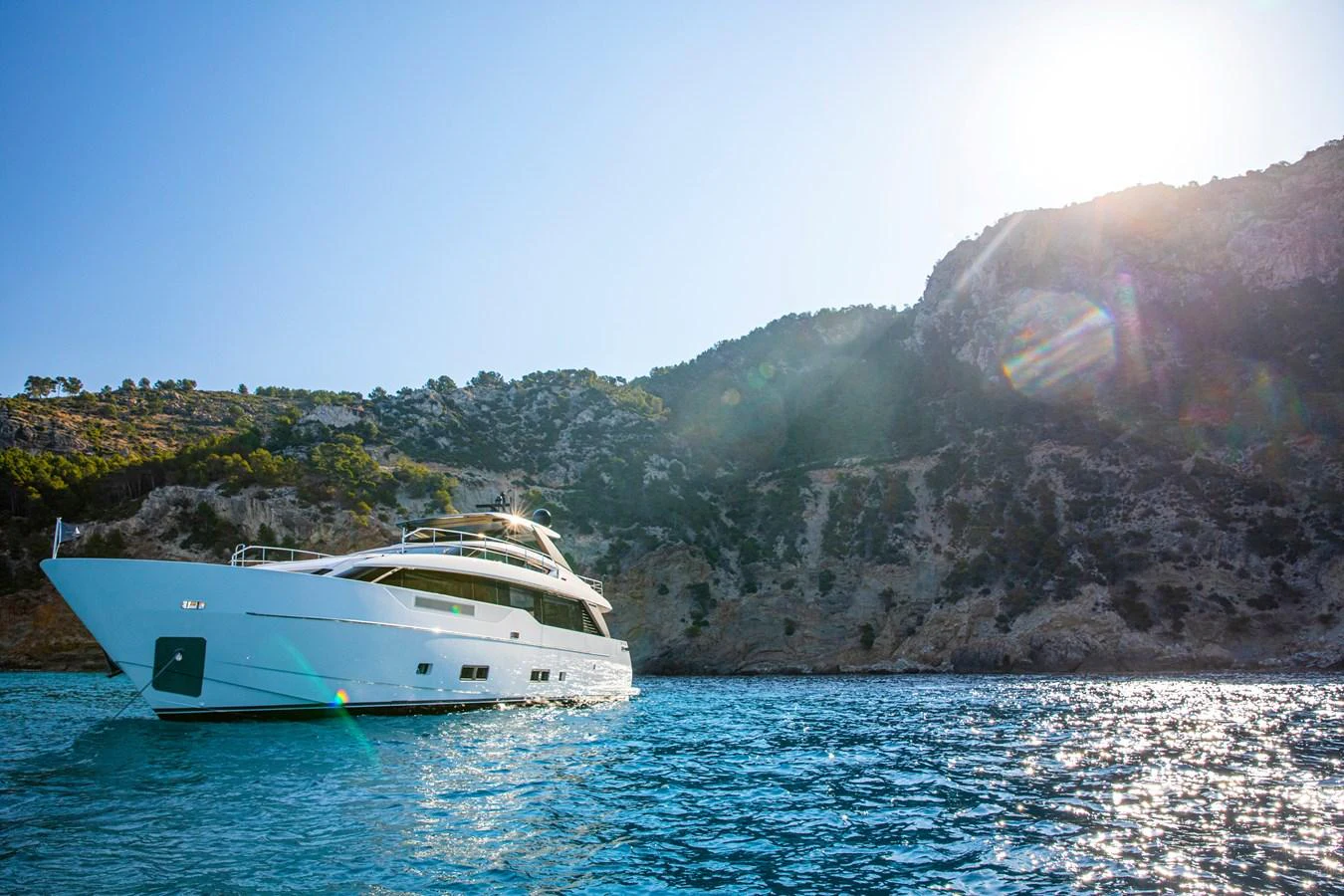 A sleek yacht cruises through clear blue waters with a scenic mountainous backdrop. aboard SEVEN Yacht for Sale