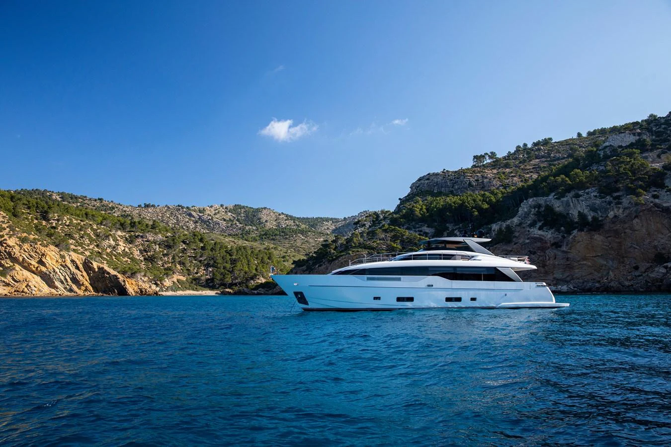 A sleek yacht cruises along a picturesque coastline under a clear blue sky. aboard SEVEN Yacht for Sale